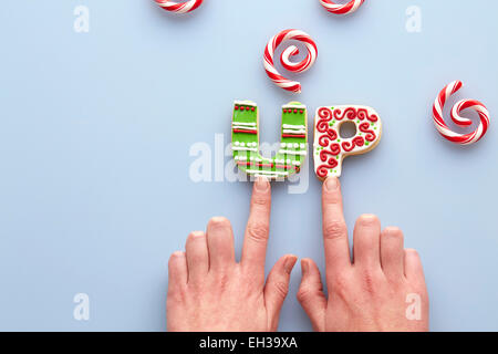 Vue de dessus de Woman's Hands et biscuits de Noël en sucre l'orthographe sur fond bleu avec des tourbillons de canne Banque D'Images