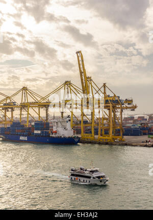 Un navire de transport de bateaux d'excursion passe et grues à conteneurs dans le Port de Barcelone ( Port de Barcelona, Puerto de Barcelona, Espagne) Banque D'Images