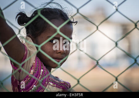 Petite fille indienne, qui vit dans la rue, se tient debout derrière une clôture à dans à l'appareil photo Banque D'Images