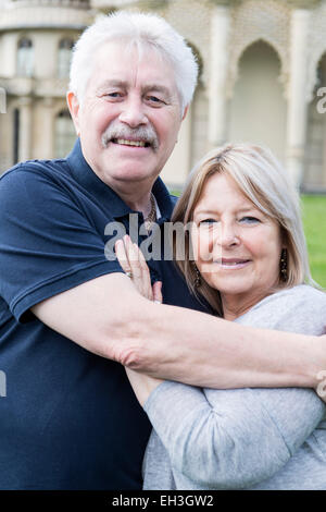 Un couple de personnes âgées câliner et embrasser montrant l'amour en face de Brighton monument touristique le Pavillon Royal sur l'herbe Banque D'Images