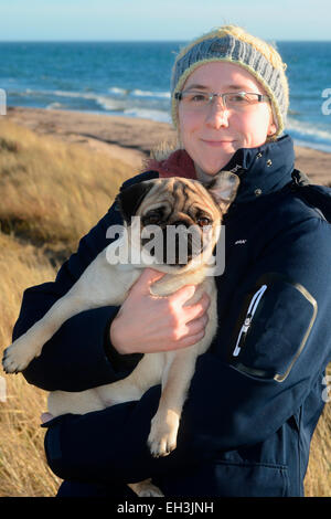 Jeune femme portant des vêtements d'hiver et la tenue d'un pug, sur la mer Baltique, Scania, Suède Banque D'Images