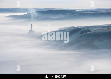 Un voile de brume sur le village de Castleton dans le Peak District. La cimenterie et sa cheminée est au-dessus de la brume. Banque D'Images