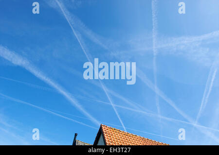 Chemtrails et trainées dans un ciel bleu au-dessus de maisons Banque D'Images