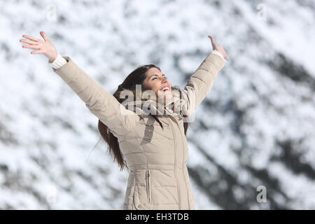 Happy woman raising arms sur les vacances d'hiver, avec la montagne enneigée en arrière-plan Banque D'Images