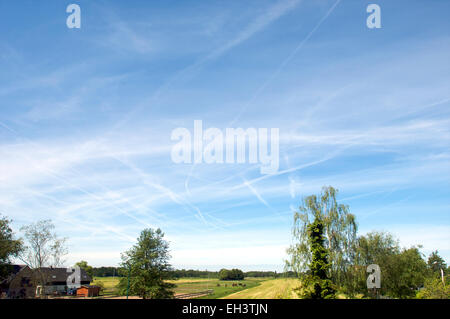 Chemtrails et trainées dans un ciel bleu au-dessus de maisons Banque D'Images