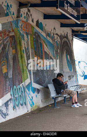 Homme assis sur le banc en face d'œuvres sur les murs de la gare à Pokesdown de Boscombe Bournemouth, Dorset, en août Banque D'Images