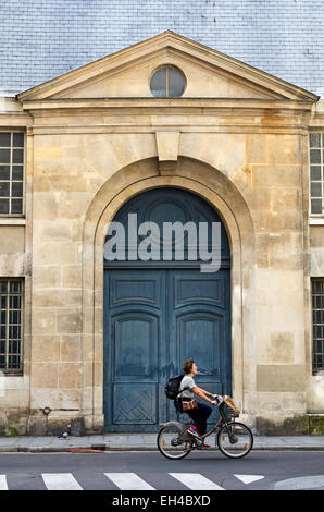 Une femme vélos devant un ancien site porte sur la Rue de vielle du Temple à Paris. Banque D'Images