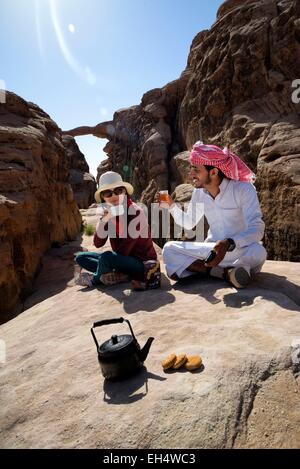 La Jordanie, Wadi Rum, zone protégée inscrite au Patrimoine Mondial de l'UNESCO, pause thé, touristique et local guide bédouin, Burdah rock bridge en arrière-plan Banque D'Images