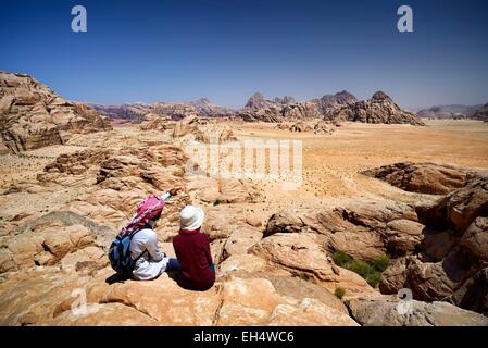 La Jordanie, Wadi Rum, zone protégée inscrite au Patrimoine Mondial de l'UNESCO, touristique et local guide bédouin assis sur un rocher, contemplant le paysage du mont Jebel Burdah Banque D'Images