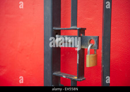 Cadenas verrouillé sur la vis en metal gate ouvert en face de red wall Banque D'Images