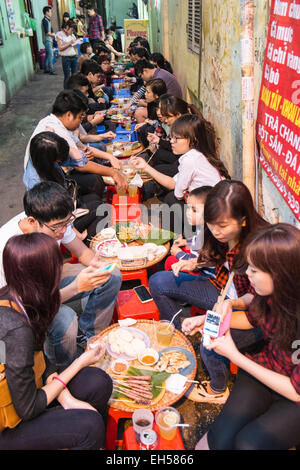 Jeunes gens assis sur des tabourets en plastique pour un repas dans l'alimentation de rue Han Noi, Hanoi, Vietnam, Banque D'Images