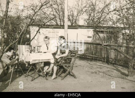 L'Allemagne. 28 Février, 2015. CIRCA 1962 : un homme avec un appareil photo sur un trépied photos de deux femmes assises à une table dans le jardin © Igor Golovniov/ZUMA/Alamy Fil Live News Banque D'Images