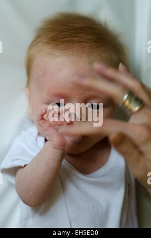 un bébé de 10 semaines joue avec le doigt de sa mère. Banque D'Images