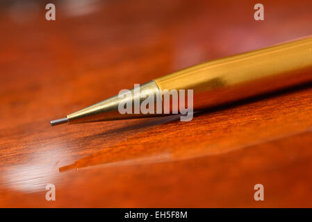 Plume d'or assis sur une texture en bois verni avec réflexion Banque D'Images