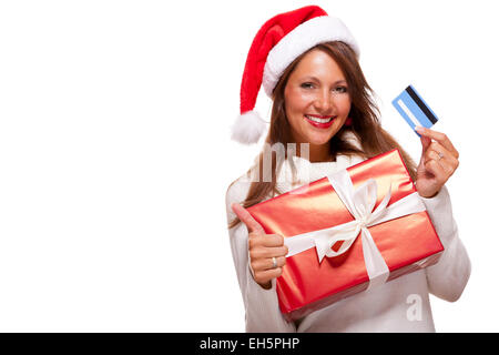 Smiling woman wearing a Santa hat rouge l'achat de cadeaux de Noël sur une carte bancaire brandissant une giftwrapped fort rouge avec un sourire heureux et un coup de geste de succès, isolated on white Banque D'Images