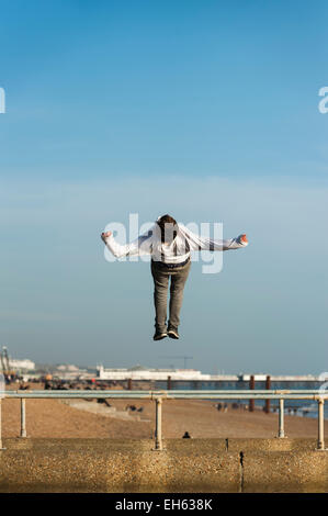 Brighton, East Sussex, UK. 7 mars 2015. Météo France : un groupe de jeunes un jeune homme fait des culbutes et retourne en arrière dans l'air alors qu'un groupe de jeunes font l'essentiel de la première journée de beau temps de printemps pratiquer l'art du parkour, free-sauter et faire des sauts périlleux, au large de la jetée sur le front de mer de Brighton à Brighton Pier en arrière-plan. Brighton, East Sussex, Angleterre, Royaume-Uni. Banque D'Images