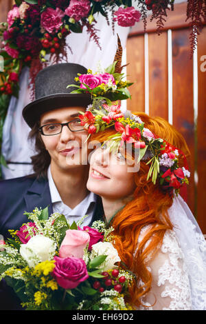 Cheerful couple marié, kissing en décorations florales. Cheveux rouge mariée. Banque D'Images