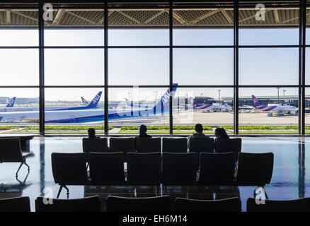 Les gens assis dans Narita Terminal 1, à l'intermédiaire de grandes fenêtres en verre sur le terminal de portes à l'Aéroport International de Narita, Japon Banque D'Images