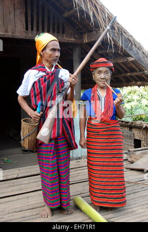 Couple portant des costumes traditionnels tribaux devant leur maison, l'homme avec l'arme à feu, tatoué, dame face Kanpetlet Village Chin Banque D'Images