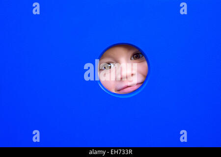 Cute little boy's face peeking through un trou d'un équipement de terrain. Banque D'Images