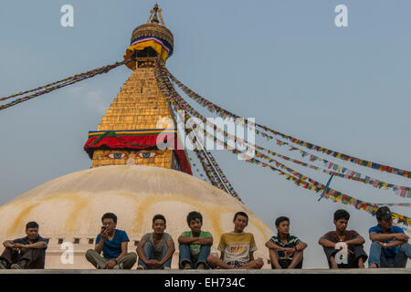 Les jeunes hommes assis en face de Bodhnath Stupa's roof au coucher du soleil avec les drapeaux de prières, Katmandou Banque D'Images