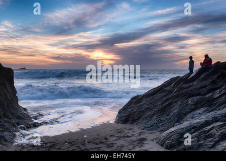 Mère et son jeune fils à regarder les vagues au coucher du soleil à peu d'une petite crique de Fistral en retrait de la plage de Fistral au-dessous de la tête de Towan Banque D'Images