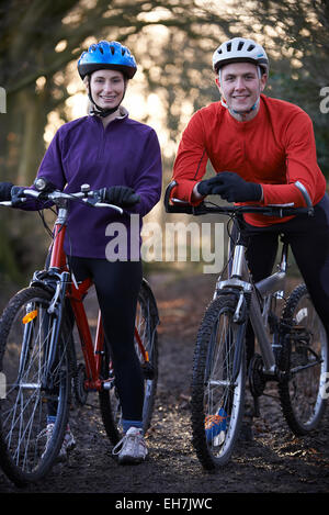Couple Riding Mountain Bikes à travers des bois Banque D'Images