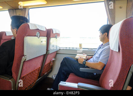 Asiatique d'âge moyen homme assis sur un train express confortable avec beaucoup de place pour les jambes au Japon. Banque D'Images