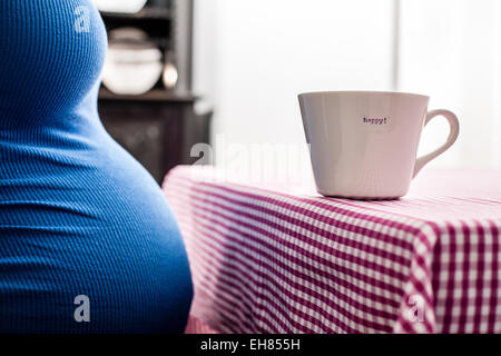 Femme en grossesse à terme complet portant un haut bleu. La tasse sur le tableau se lit avec plaisir. Banque D'Images