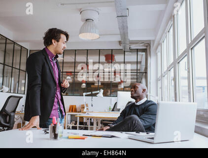 Deux jeunes employés de bureau ayant une réunion à 24. Mixed Race business people discussing work in office. Banque D'Images