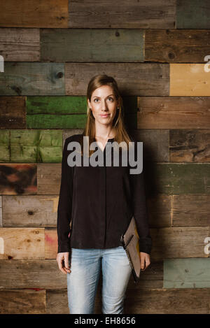 Portrait de belle jeune businesswoman standing contre un mur en bois à la recherche de l'appareil photo. Caucasian woman in casuals in office Banque D'Images