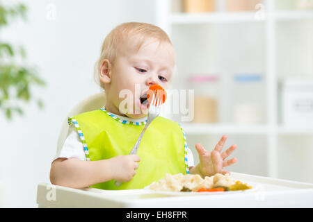 Bébé garçon dans une chaise haute pour l'alimentation à l'aide d'une fourchette et une assiette je Banque D'Images