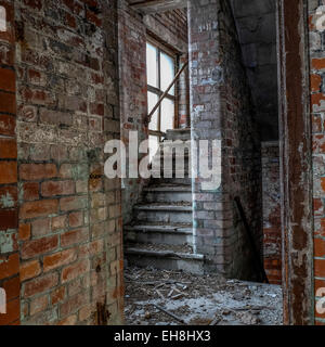 Escalier ancien dans une usine désaffectée avec main courante et les débris sur le sol. Banque D'Images