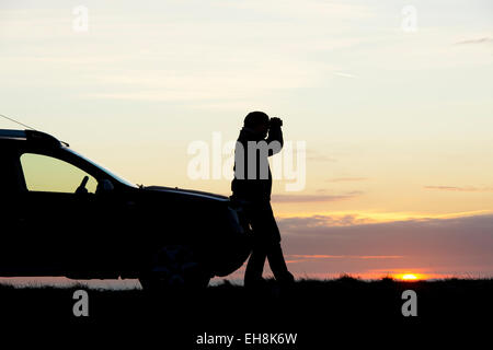 L'homme à la silhouette avec des jumelles à côté d'une voiture 4X4 au lever du soleil. UK Banque D'Images