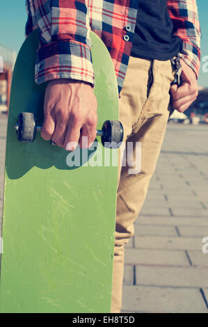 Un jeune homme avec une chemise à carreaux avec une planche à roulettes à la main verte Banque D'Images