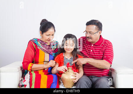 3 Indian grand parents et grand enfant fille assis canapé Tirelire d'économiser de l'argent Banque D'Images