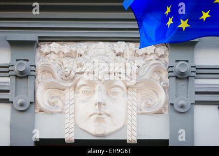 Bas-relief de la tête d'une femme sur le mur d'une vieille maison et le drapeau de l'UE dans la vieille ville. Riga, Lettonie Banque D'Images