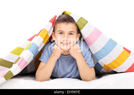 Petit garçon allongé sur un lit recouvert d'une couverture isolé sur fond blanc Banque D'Images