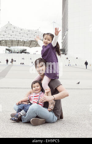 Père assis sur le sol avec deux enfants dans la ville Banque D'Images