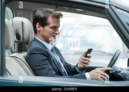 L'homme à la recherche de téléphone cellulaire au volant Banque D'Images