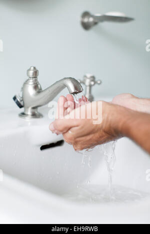 L'homme prenant les mains sous l'eau qui coulait du robinet de salle de Banque D'Images