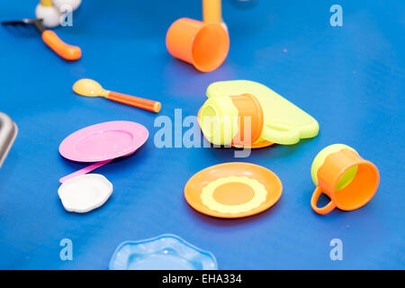 Des assiettes, des cuillères et des tasses, des jouets éparpillés sur un sol bleu. Banque D'Images