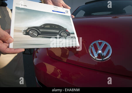 Orange County, Californie, USA. 13 Oct, 2011. Les mains d'un homme peut être vu la tenue d'une Volkswagen Beetle 2012 brochure de ventes aux côtés de l'avant d'une rouge 2012 VW bug avec une médaille d'enjoliveur de capot. © David Bro/ZUMA/Alamy Fil Live News Banque D'Images