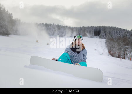 Jeune femme assise avec snowboard dans la neige sur la montagne Banque D'Images
