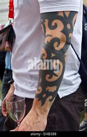 Un homme avec un bras tatoués tenant un verre de vin vide Banque D'Images
