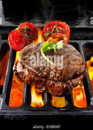 Steaks de boeuf et les tomates en cours de cuisson sur un feu ouvert grill Banque D'Images