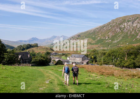 Deux promeneurs marchant sur colline en village avec vue de Snowdon à distance dans le parc national de Snowdonia (Eryri). Capel Curig Conwy Wales Royaume-uni Grande-Bretagne Banque D'Images