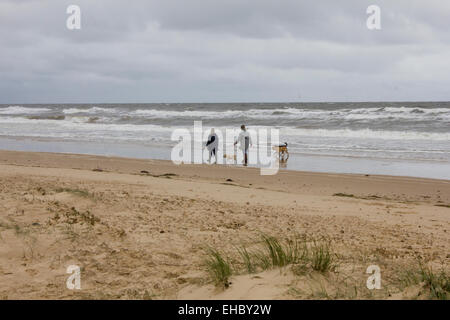 Les gens qui marchent avec leurs chiens sur une plage déserte à Holkham North Norfolk par un jour de vent et de nuages lourds avec une mer sauvage. Banque D'Images