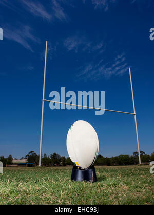 Ballon de rugby est assis sur un tee, prêt à être frappé par les poteaux de but, avec un ciel bleu en arrière-plan. Banque D'Images