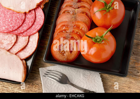 Divers Les saucisses et les tomates sur des assiettes en céramique noire Banque D'Images